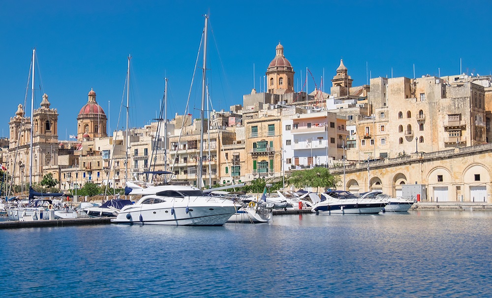 Widok na zabudowę z jasnego piaskowca stolicy Malty, od strony morza. Na pierwszym tle przystań z jachtami